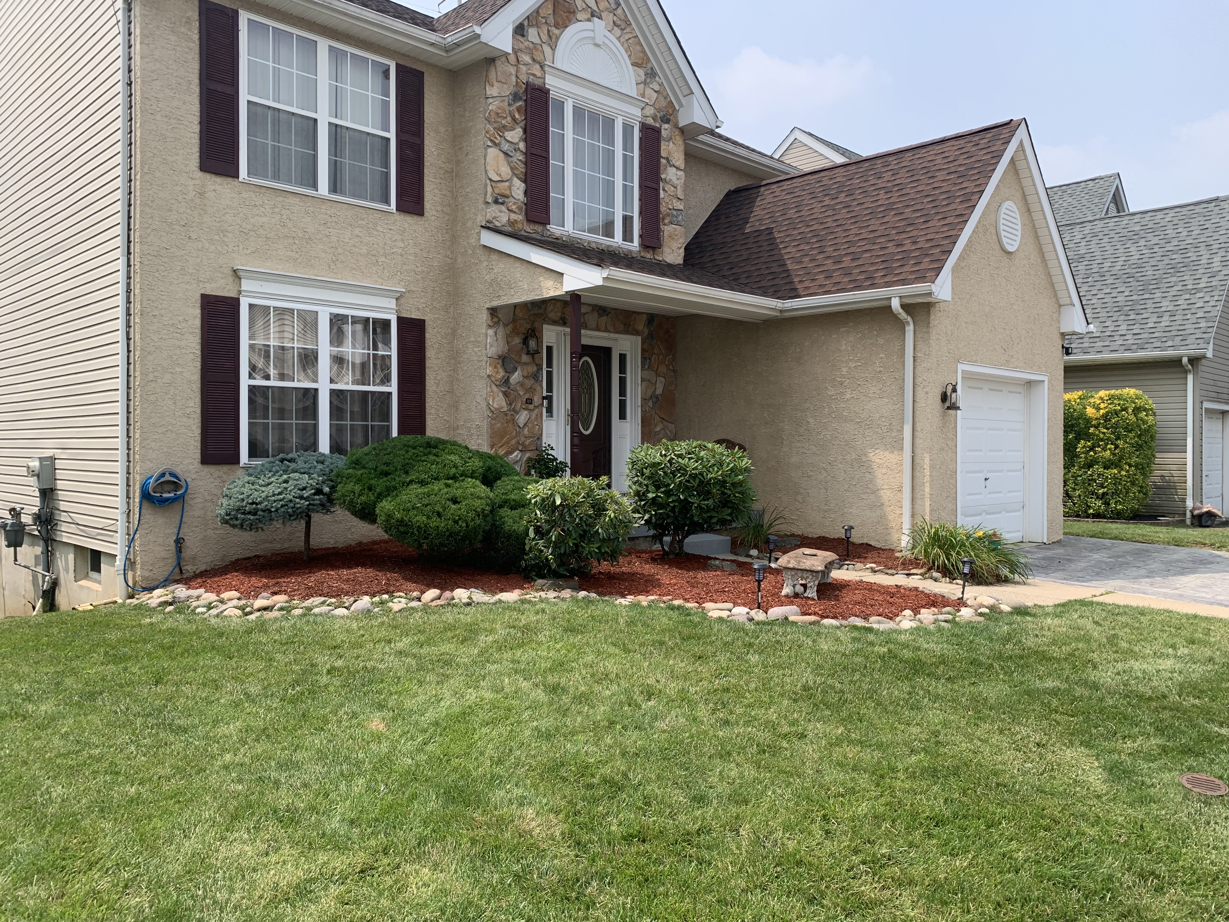 Front yard with red mulch, river rock border, and shaped shrubs